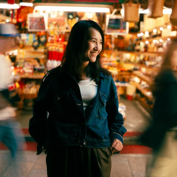 Traveler smiling on Jiufen's Jishan Street at night while passers-by blur past in motion