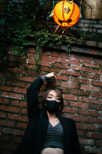 Low-angle portrait of a traveler against a red-brick wall under a single lantern in Jiufen